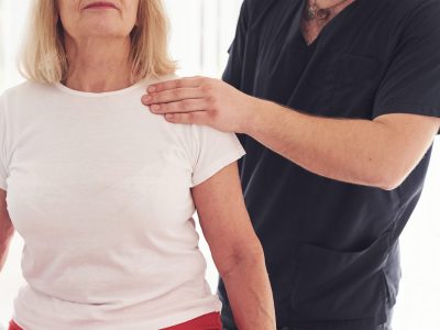 Older woman have a visit in clinic and having rehabilitation. Male instructor helping her.